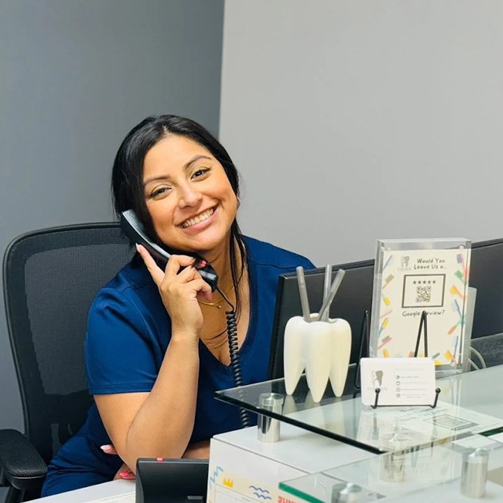 Reina, the friendly office manager at Karande Dental Care, smiling while speaking with a patient at the front desk